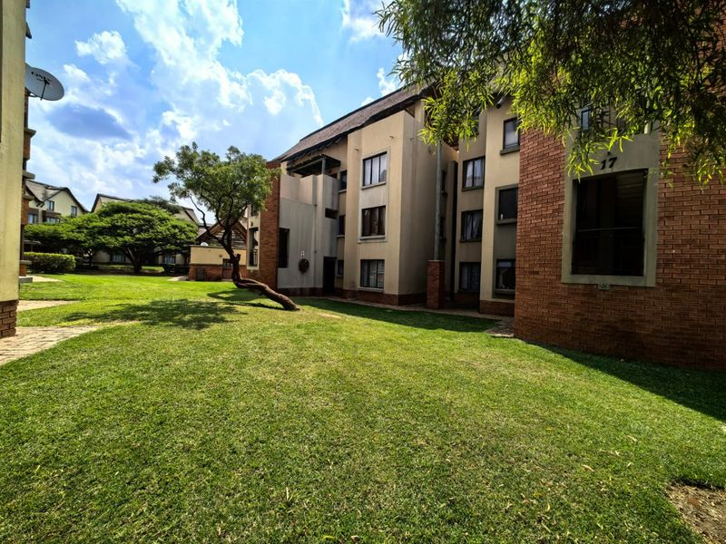 A view of the rear exterior of the apartment complex, featuring brick facade detailing, established communal gardens, and multiple residential balconies.