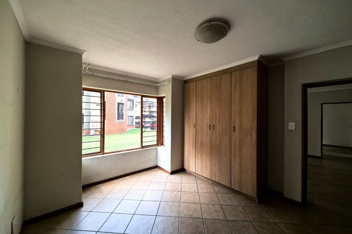 A vacant bedroom featuring tiled flooring, built-in wooden cupboards, and large windows with security bars, offering a functional and neutral living space.