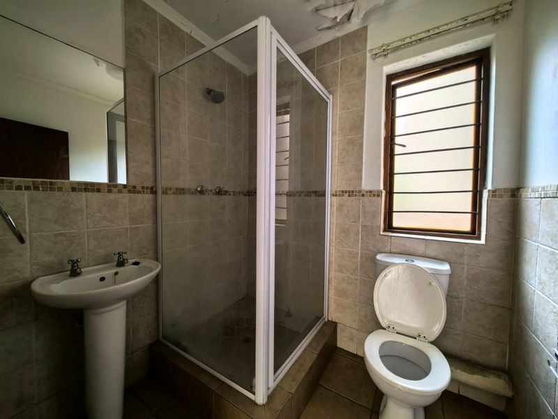A dated bathroom featuring a pedestal basin, shower enclosure, and toilet, requiring maintenance and cosmetic updates to the ceiling and finishes.
