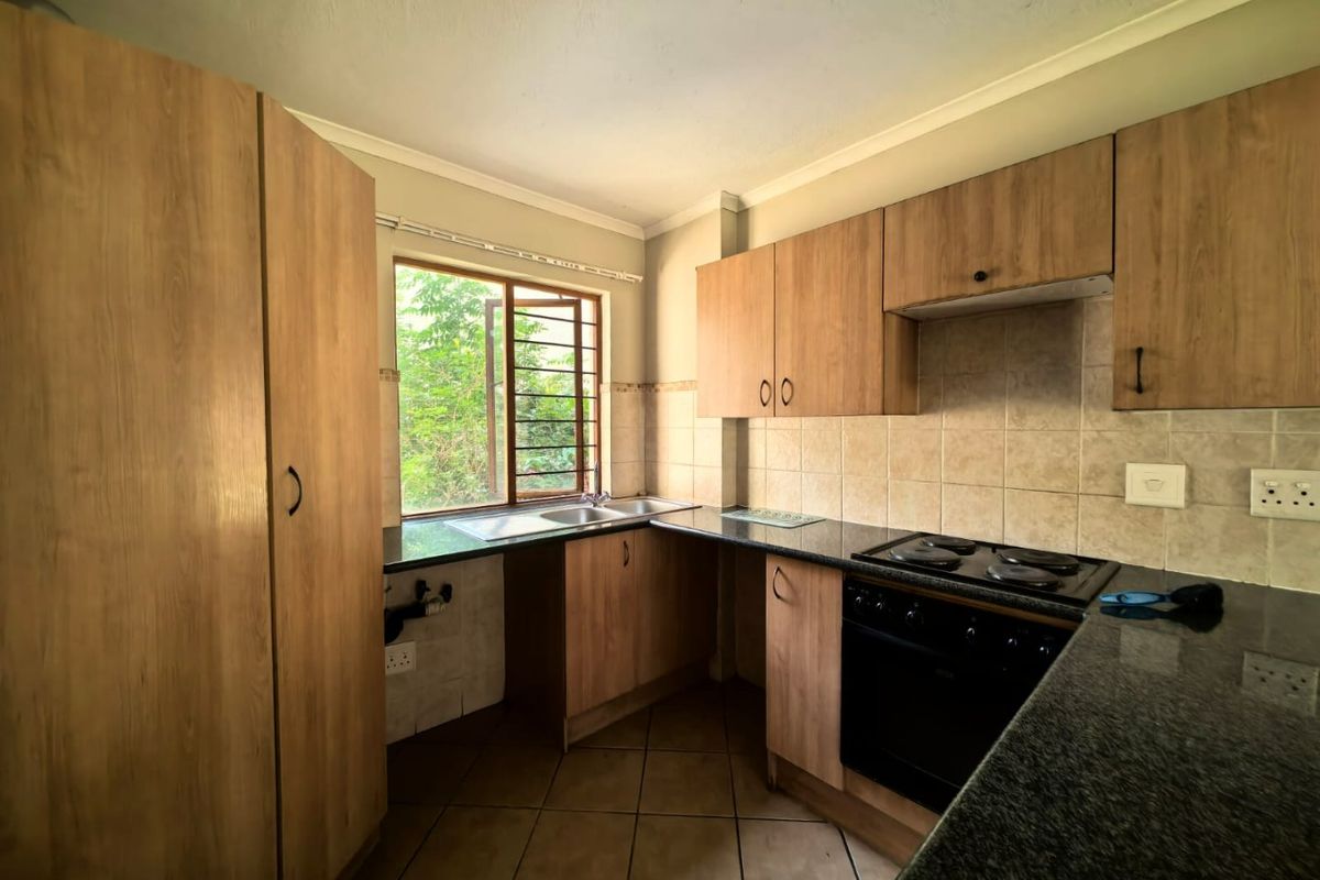 A functional kitchen featuring wood-look cabinetry, granite countertops, a built-in oven and hob, and tiled flooring, offering a practical layout for daily use.