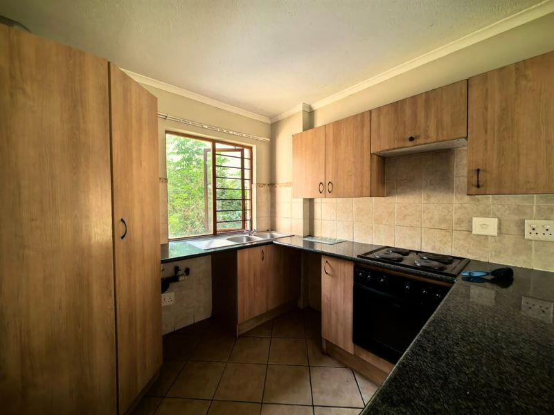 A functional kitchen featuring wood-look cabinetry, granite countertops, a built-in oven and hob, and tiled flooring, offering a practical layout for daily use.