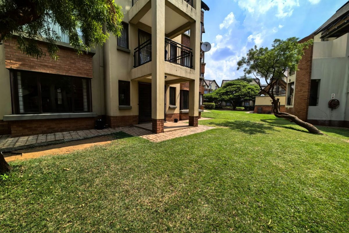 Rear view of the apartment building featuring a brick facade, private balcony, paved patio area, and well-maintained communal garden space.