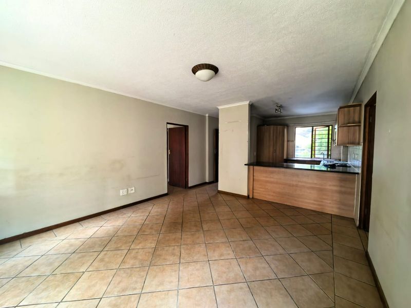 An open-plan living and kitchen area featuring tiled flooring, a breakfast bar with granite countertops, and neutral wall finishes.