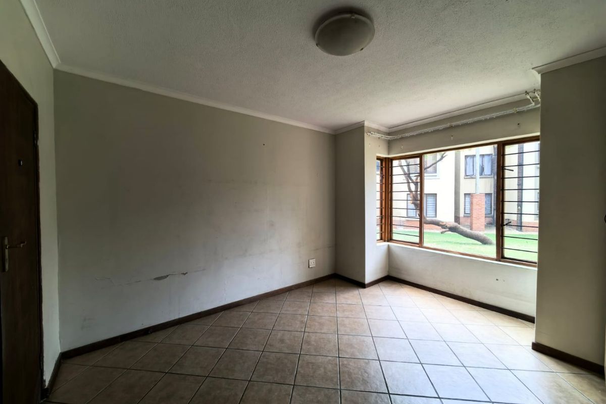 An empty living room featuring tiled flooring, large windows with security bars, and neutral wall finishes in need of minor cosmetic repair.