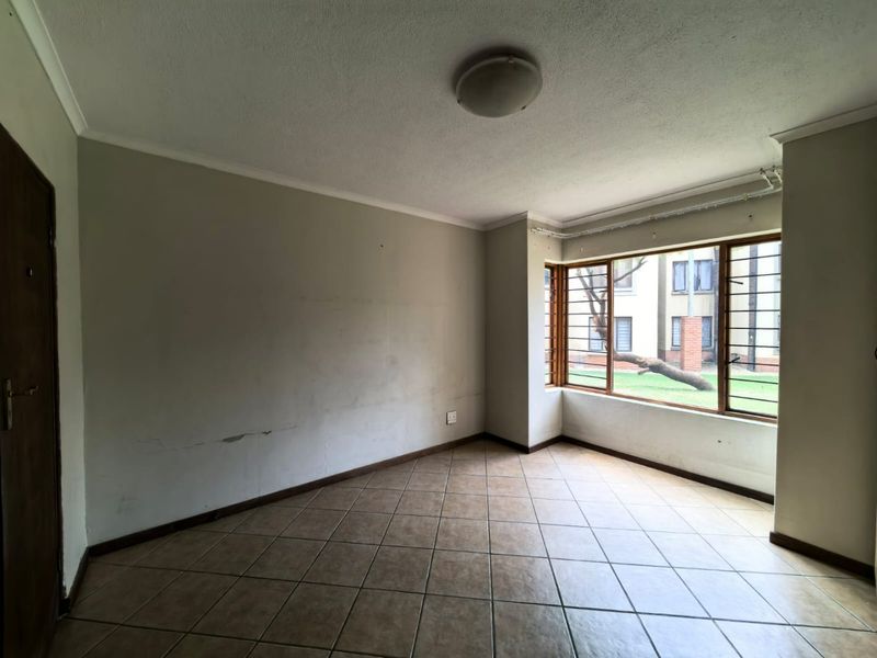 An empty living room featuring tiled flooring, large windows with security bars, and neutral wall finishes in need of minor cosmetic repair.