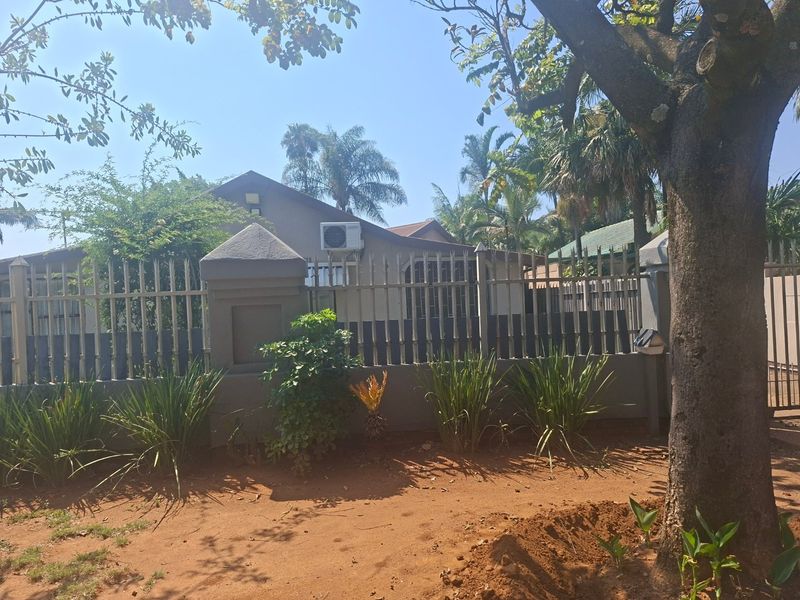 Front view of the property featuring a secure metal perimeter fence with masonry pillars and established garden landscaping.