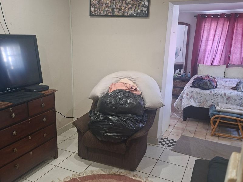 A living area with tiled flooring, leading into an adjacent bedroom space.