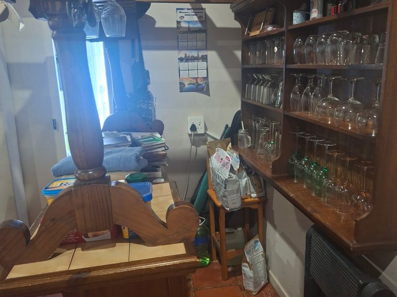 A rustic home bar area featuring built-in wooden cabinetry, shelving for glassware, and traditional terracotta floor tiles with exposed ceiling beams.