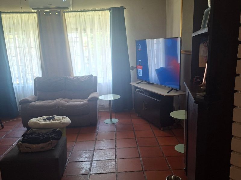 A living room featuring terracotta floor tiles, a timber slat ceiling, and a wall-mounted air conditioning unit.