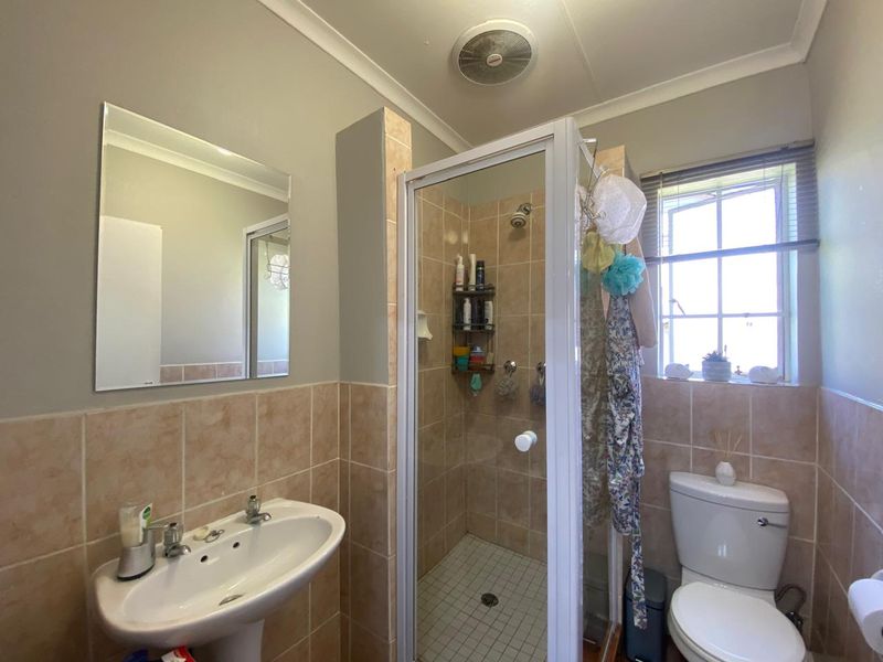 A functional bathroom featuring a pedestal basin, a glass-enclosed shower, and a toilet, finished with neutral wall and floor tiling.