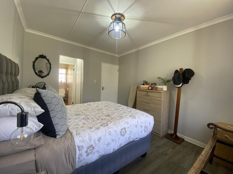 A well-maintained bedroom featuring laminate flooring, neutral wall tones, and a modern industrial-style ceiling light fixture, with an adjoining en-suite bathroom.