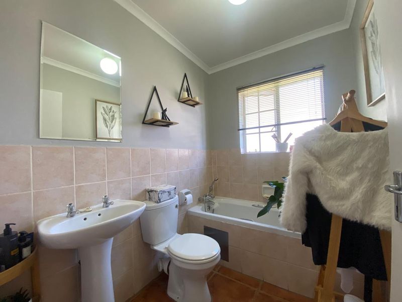 A functional bathroom featuring a pedestal basin, toilet, and bathtub with tiled splashbacks and flooring, offering a clean and practical layout.