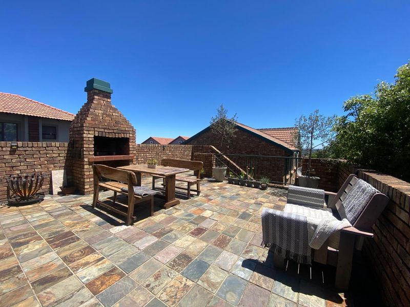 Spacious outdoor patio featuring a built-in brick braai, stone tile flooring, and perimeter brick walls, ideal for entertaining.