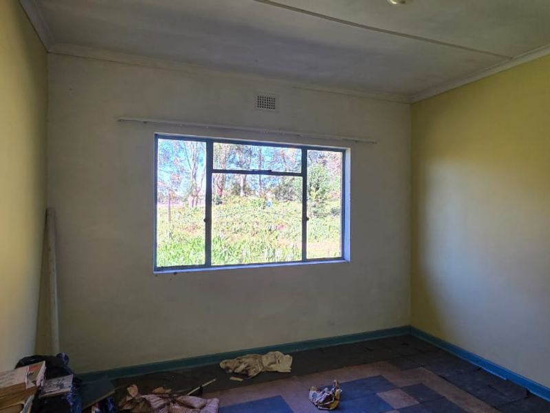 A vacant bedroom featuring built-in shelving and a large window, requiring cosmetic updates and flooring replacement to restore its appeal.