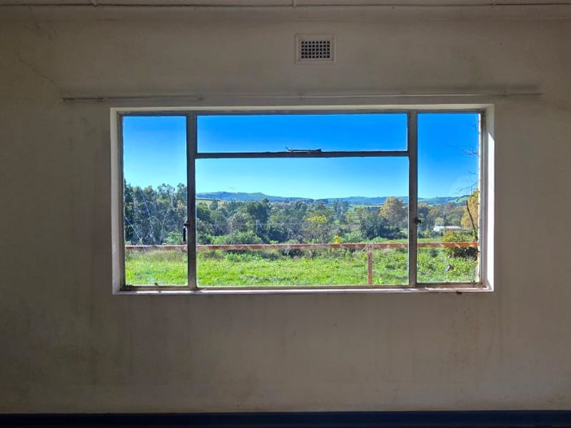 An empty bedroom featuring a large steel-framed window with scenic landscape views, requiring cosmetic updates to the wall finishes.