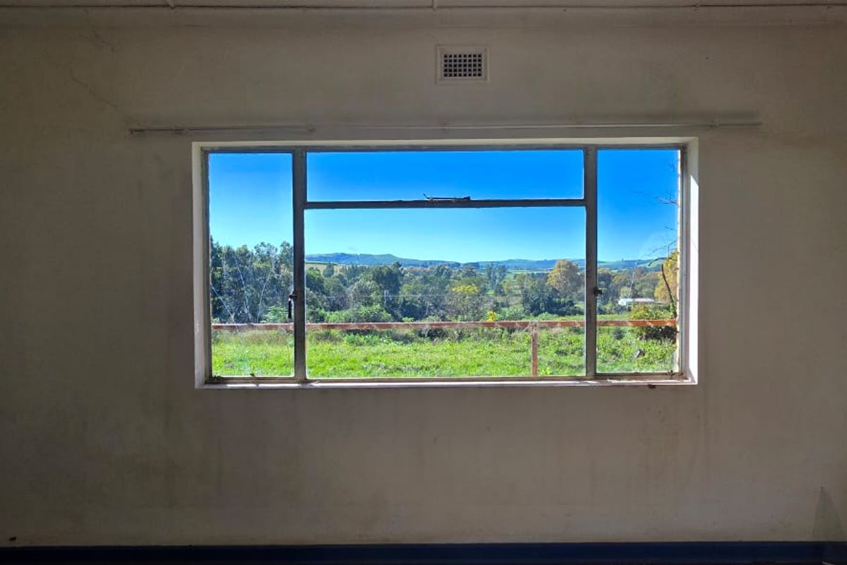 An empty bedroom featuring a large steel-framed window with scenic landscape views, requiring cosmetic updates to the wall finishes.