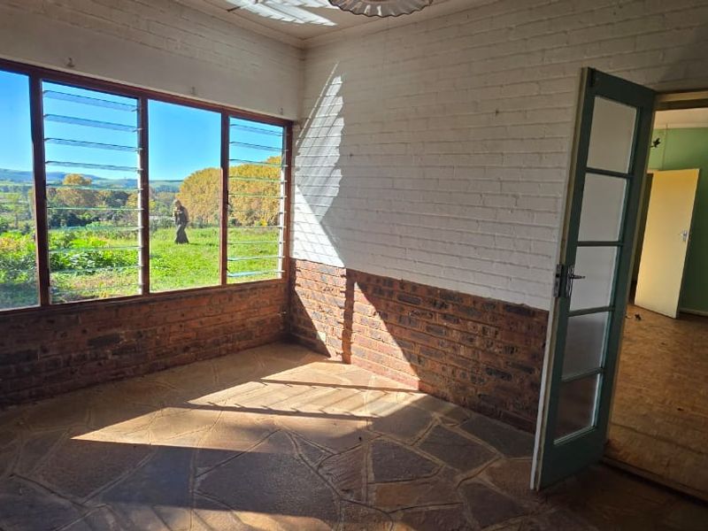 A sunlit enclosed patio featuring exposed brick walls, stone flooring, and large louvre windows offering scenic views of the surrounding landscape.