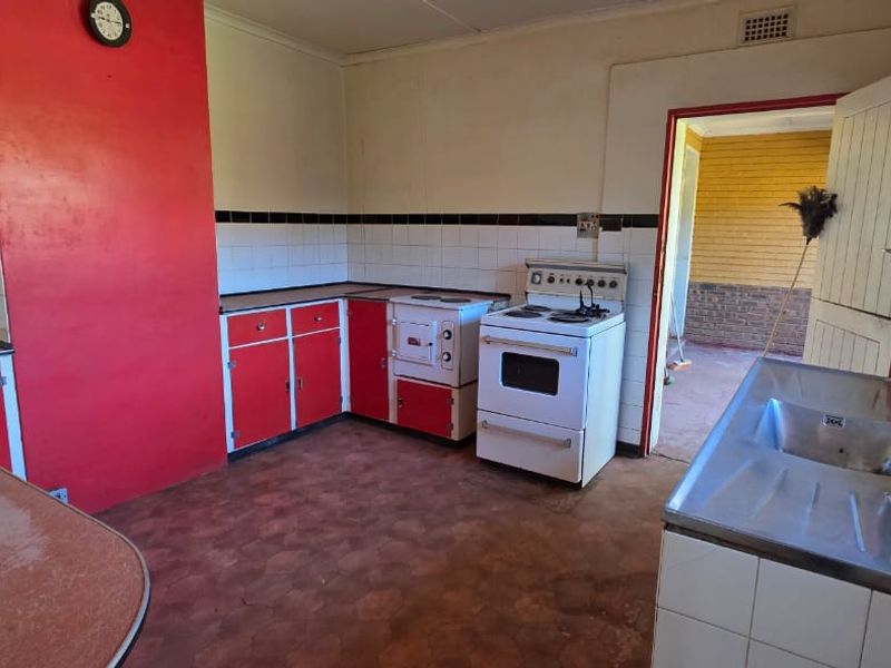 A dated kitchen featuring red cabinetry, a stainless steel sink, and a freestanding stove, offering a blank canvas for a modern renovation.
