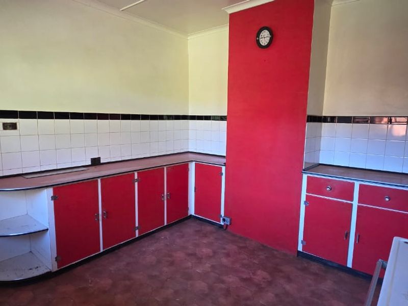 A dated kitchen featuring red and white cabinetry, tiled backsplash, and an electric stove, offering a blank canvas for modern renovation.
