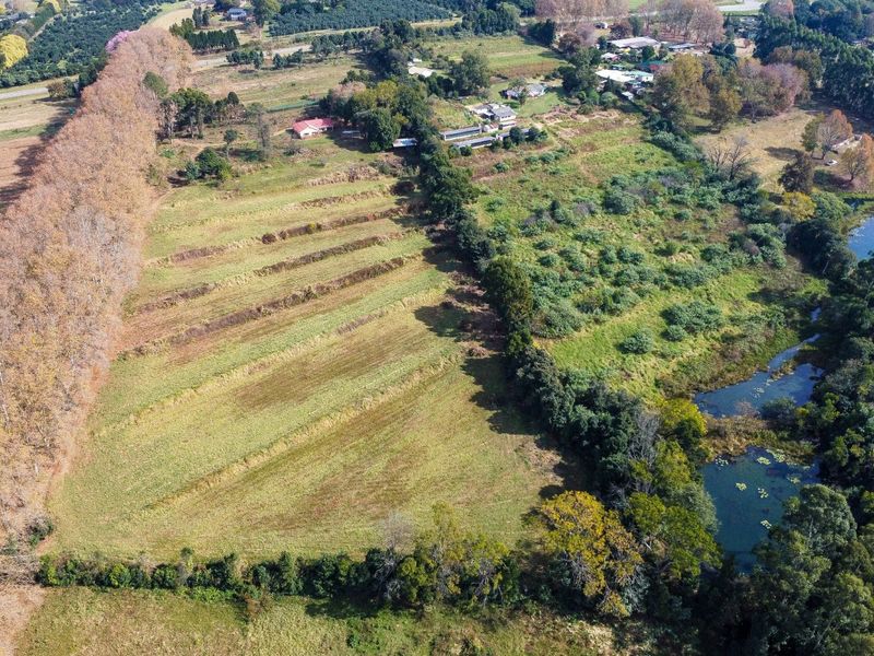 Aerial view of the small holding property featuring expansive pasture land, established tree lines, and a natural water feature.