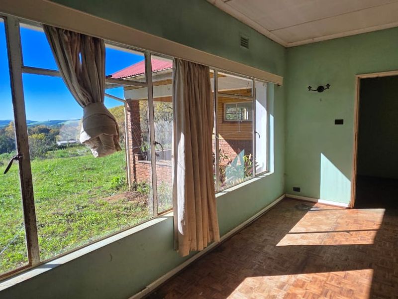 An empty living room featuring original parquet flooring, large steel-framed windows with garden views, and direct access to the rest of the home.