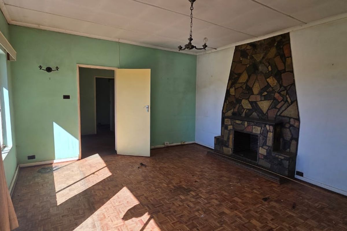 Spacious living room featuring original parquet flooring and a prominent stone fireplace, offering a blank canvas for renovation and modernization.