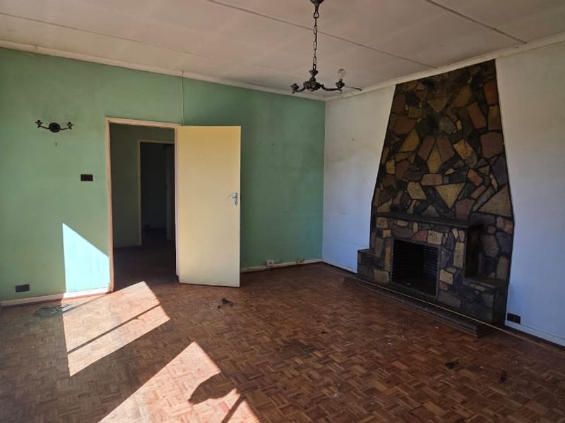 Spacious living room featuring original parquet flooring and a prominent stone fireplace, offering a blank canvas for renovation and modernization.