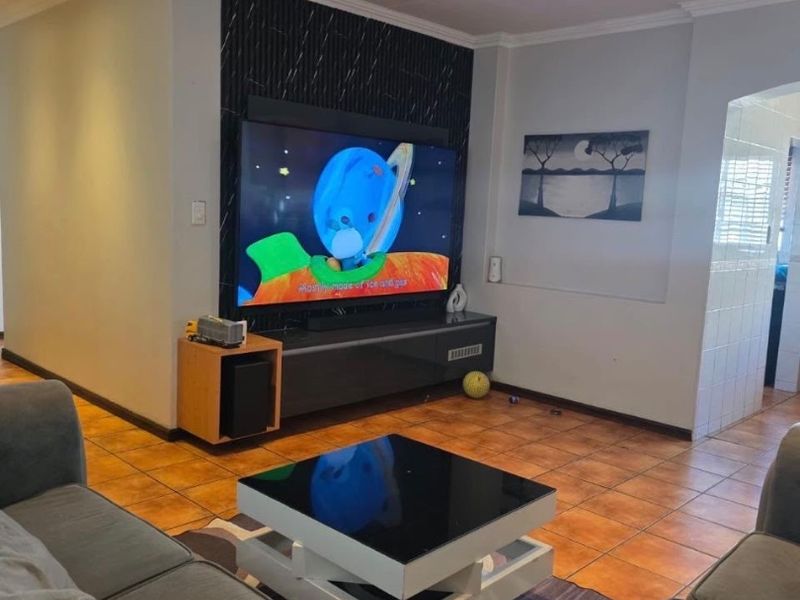 A comfortable living room featuring tiled flooring, recessed downlighting, and a modern feature wall with integrated media space.
