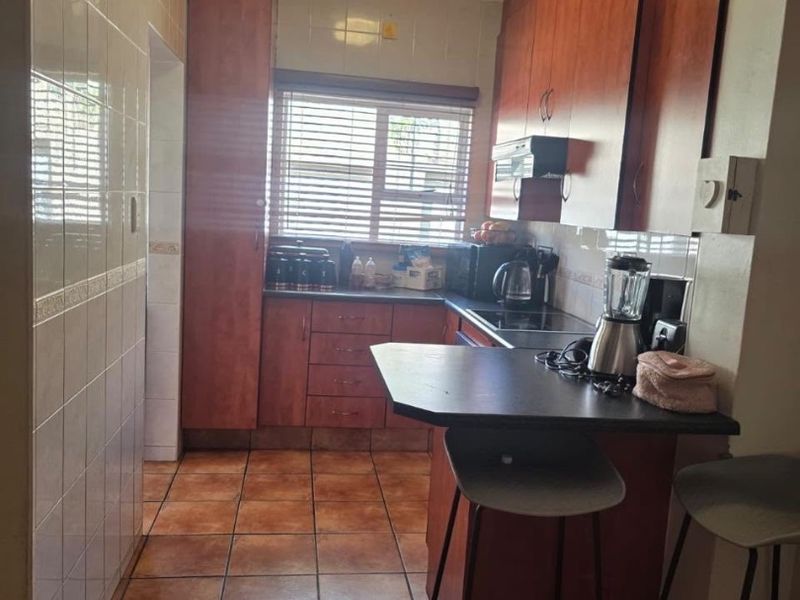 A functional kitchen featuring wood-finish cabinetry, dark countertops, a breakfast nook, and tiled flooring, offering a practical layout for daily meal preparation.