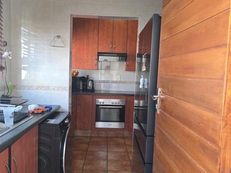A functional kitchen featuring wooden cabinetry, built-in oven and hob, tiled backsplash, and tiled flooring, providing a practical workspace.