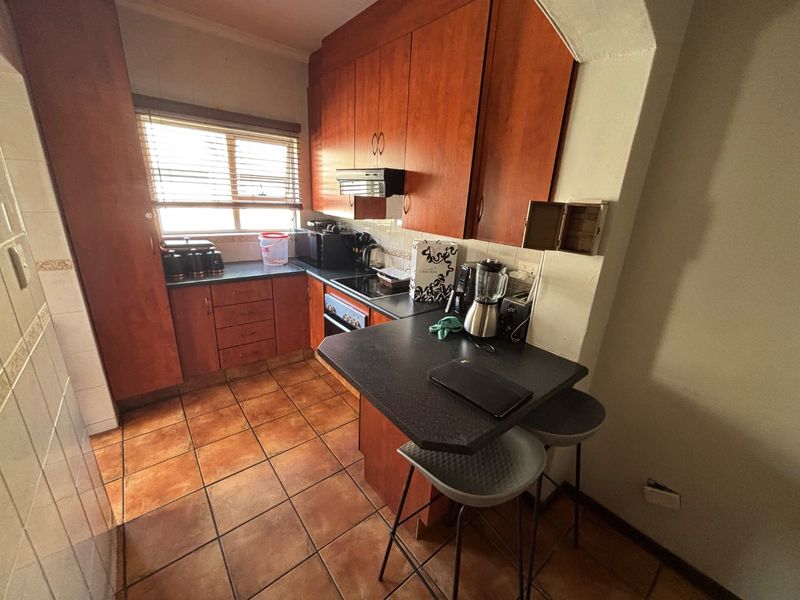 A functional kitchen featuring wooden cabinetry, dark laminate countertops, a breakfast bar, and ceramic floor tiles, offering a practical layout for daily use.