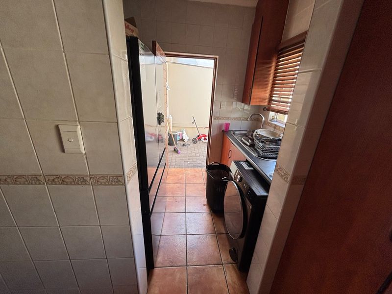 A functional laundry area featuring tiled walls and flooring, built-in cabinetry, and a stainless steel sink with direct access to an outdoor space.