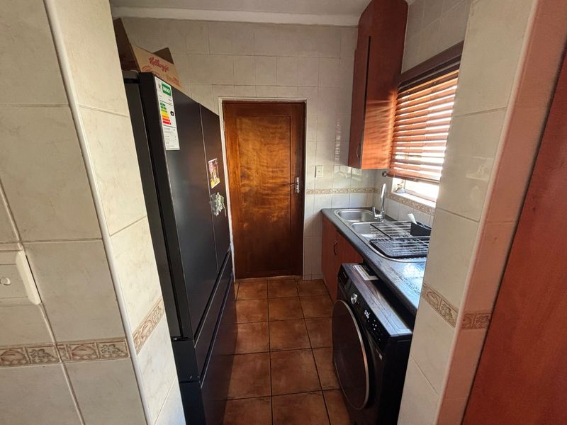 A functional scullery area featuring tiled walls, built-in cabinetry, a stainless steel sink, and dedicated space for laundry appliances.