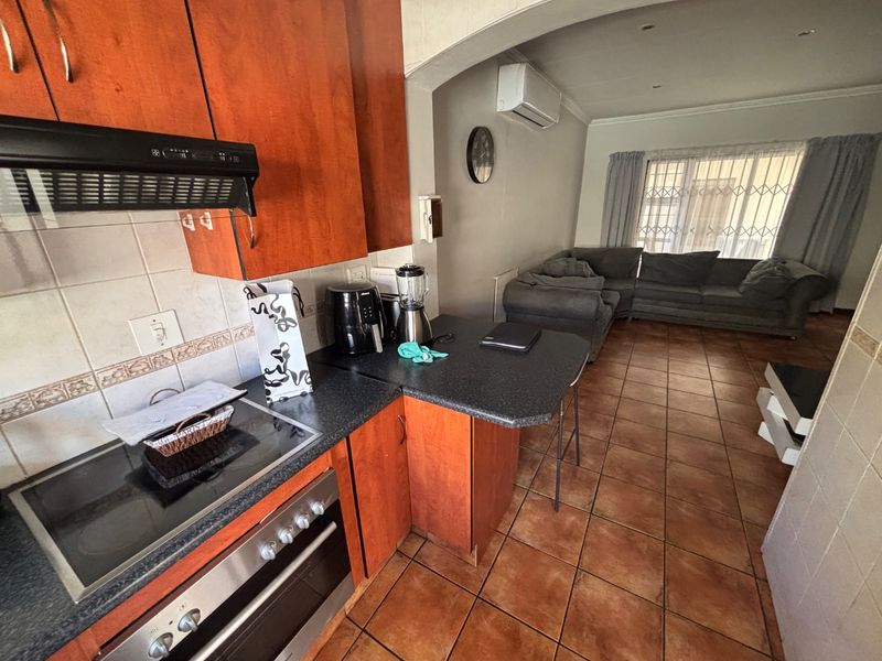 Open-plan kitchen and living area featuring wooden cabinetry, built-in oven and hob, tiled flooring, and an air conditioning unit.