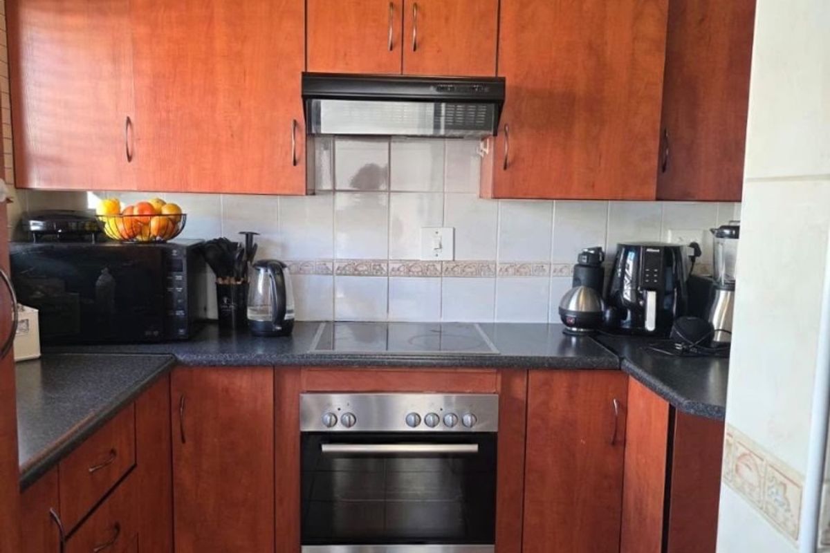 A functional kitchen featuring warm-toned wooden cabinetry, dark laminate countertops, a tiled backsplash, and integrated stainless steel oven and cooktop appliances.