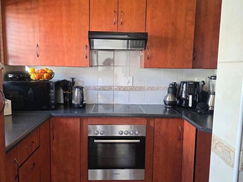 A functional kitchen featuring warm-toned wooden cabinetry, dark laminate countertops, a tiled backsplash, and integrated stainless steel oven and cooktop appliances.