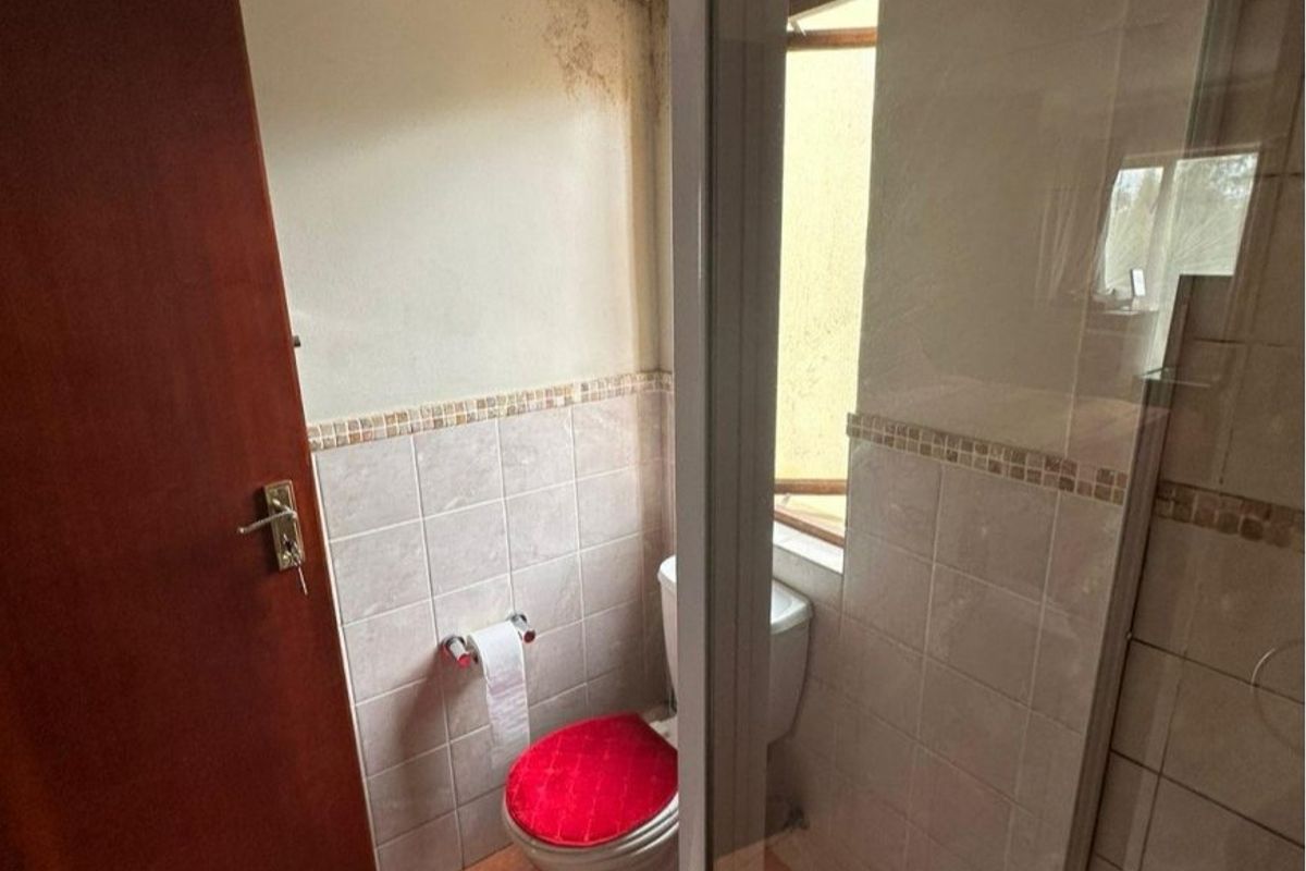 A compact bathroom featuring a shower enclosure, toilet, and tiled finishes, currently showing signs of water damage on the walls and ceiling.