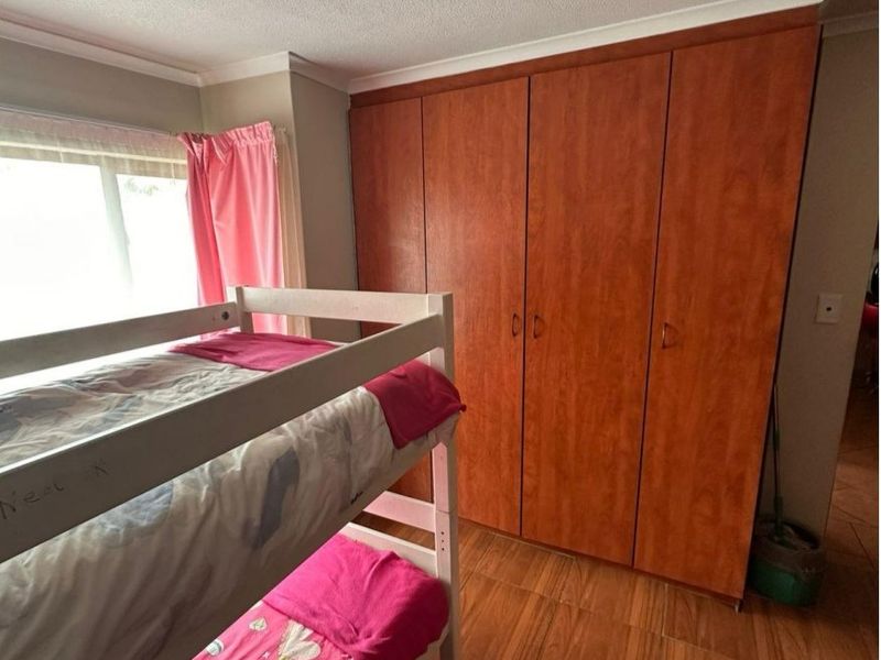 A bedroom featuring wood-look laminate flooring and floor-to-ceiling built-in cupboards with a warm wood finish.
