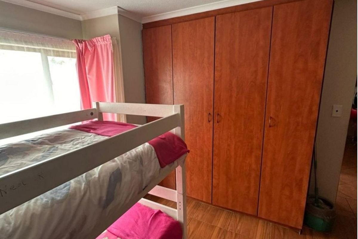 A bedroom featuring wood-look laminate flooring and floor-to-ceiling built-in cupboards with a warm wood finish.
