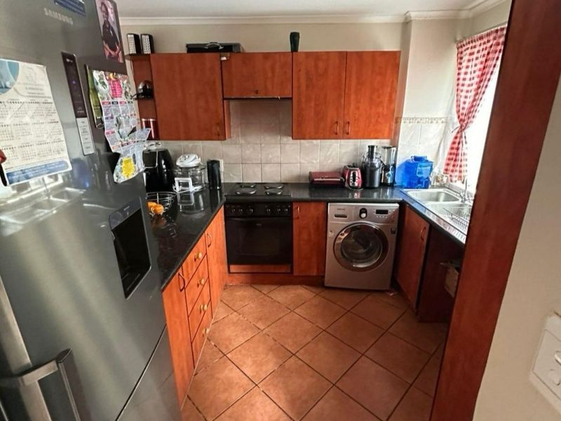 A functional kitchen featuring wood-finish cabinetry, dark countertops, tiled flooring, and integrated appliances, offering a practical layout for daily cooking and preparation.