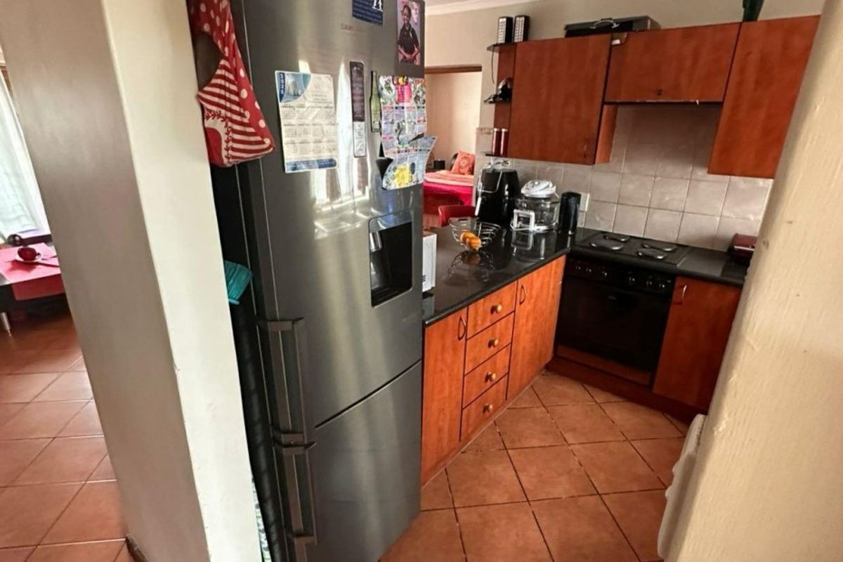 A functional kitchen featuring wooden cabinetry, dark countertops, built-in oven and hob, and tiled flooring, offering a practical layout for daily meal preparation.