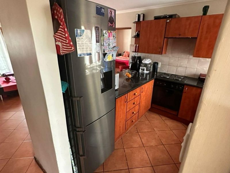 A functional kitchen featuring wooden cabinetry, dark countertops, built-in oven and hob, and tiled flooring, offering a practical layout for daily meal preparation.
