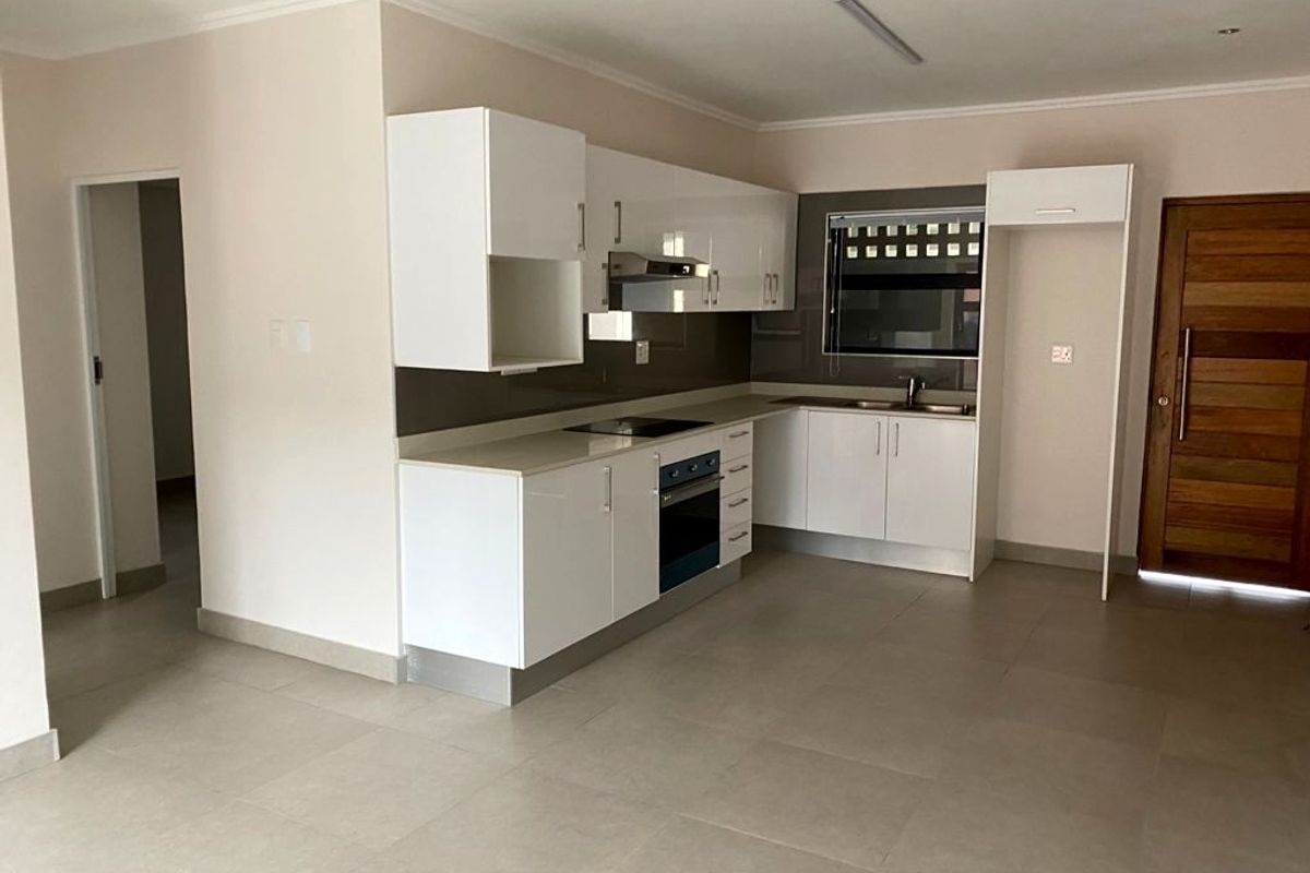 Modern kitchen featuring white high-gloss cabinetry, stone countertops, integrated oven, electric hob, and stainless steel sink, set within an open-plan living space.