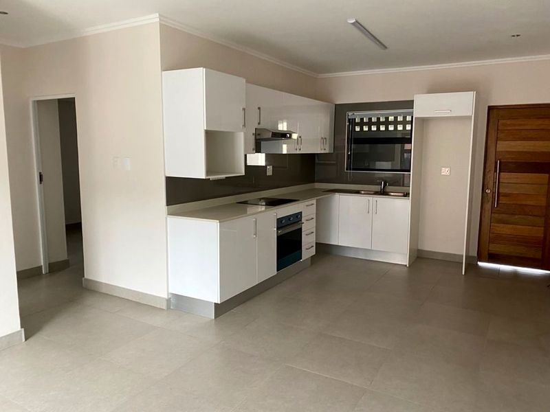 Modern kitchen featuring white high-gloss cabinetry, stone countertops, integrated oven, electric hob, and stainless steel sink, set within an open-plan living space.