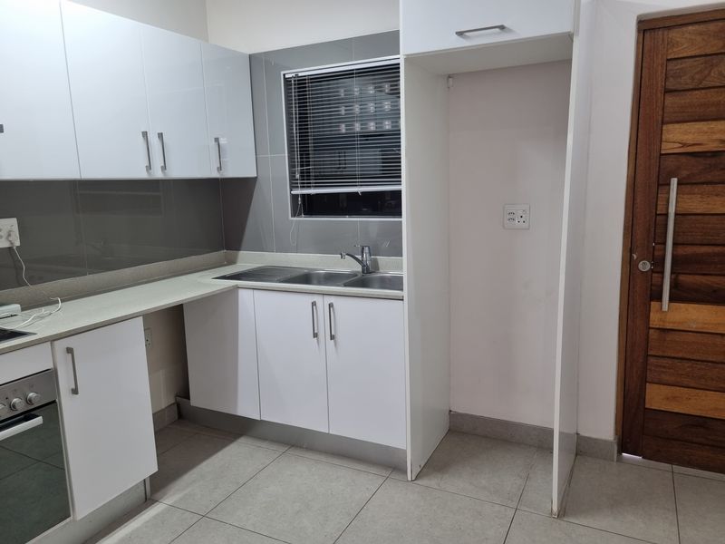 Modern kitchen featuring white cabinetry, tiled backsplash, stainless steel sink, and built-in oven, offering a clean and functional space.