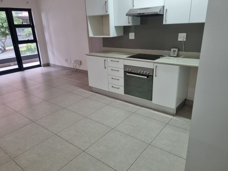 Modern open-plan kitchen featuring white cabinetry, integrated oven and hob, and tiled flooring, seamlessly connected to an outdoor access point.