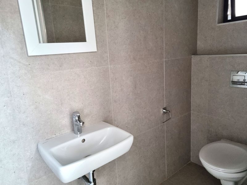 A modern, minimalist bathroom featuring neutral wall tiles, a wall-mounted basin with chrome mixer, and a wall-hung toilet with a concealed cistern.