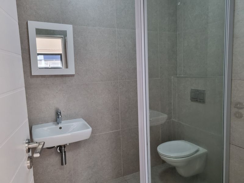 Modern bathroom featuring a wall-mounted basin, wall-hung toilet with concealed cistern, and a glass-enclosed shower, finished with neutral grey porcelain wall tiles.