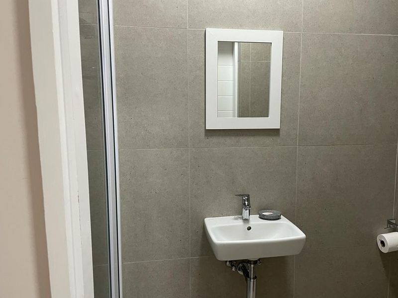 A modern bathroom featuring neutral wall tiles, a wall-mounted basin with chrome fixtures, and a glass-enclosed shower area.