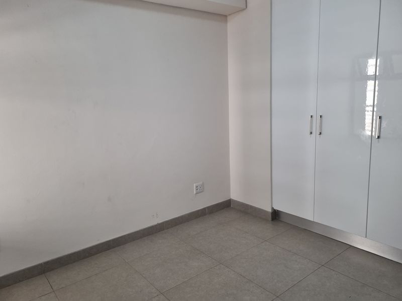 A clean, empty bedroom featuring neutral tiled flooring and modern white built-in cupboards.
